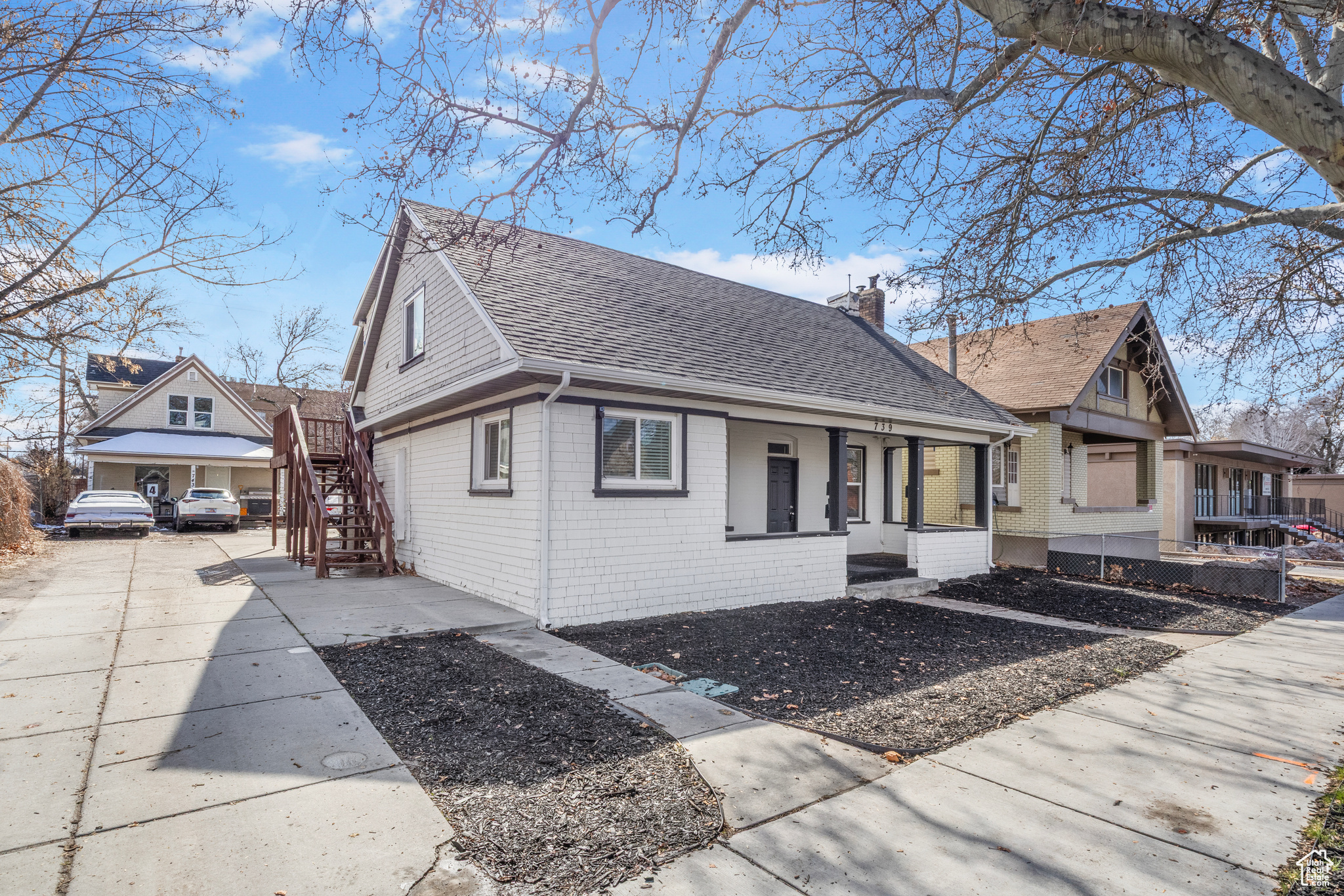 View of home's exterior featuring a shingled roof, a porch, brick siding, and a chimney