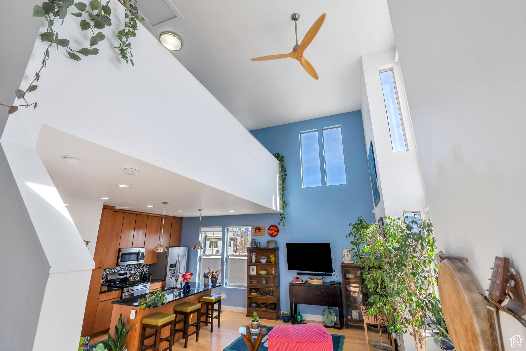 Living room with a ceiling fan, a high ceiling, recessed lighting, and light wood-style floors