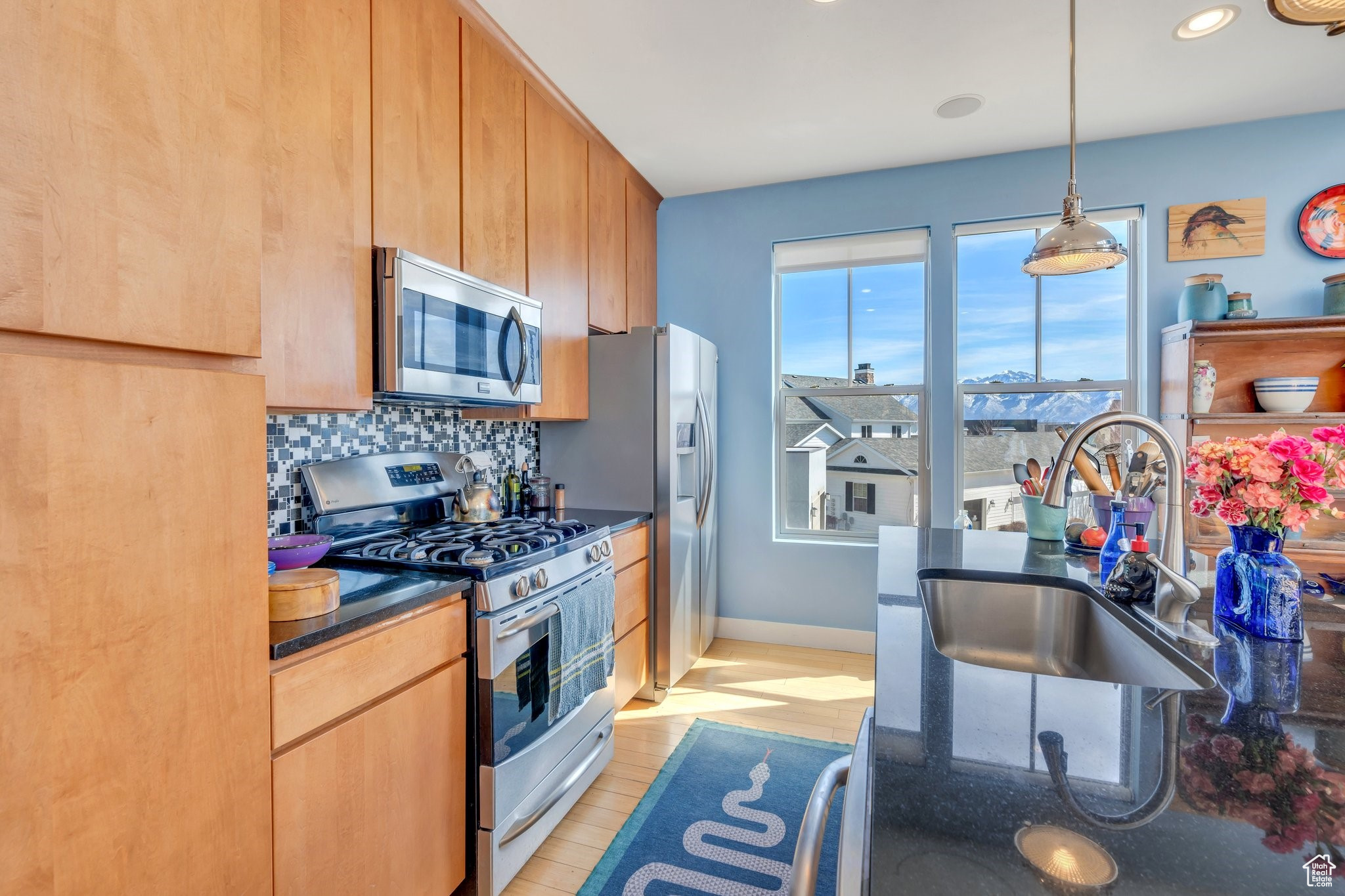 Kitchen featuring decorative light fixtures, decorative backsplash, appliances with stainless steel finishes, light wood-style floors, and a sink