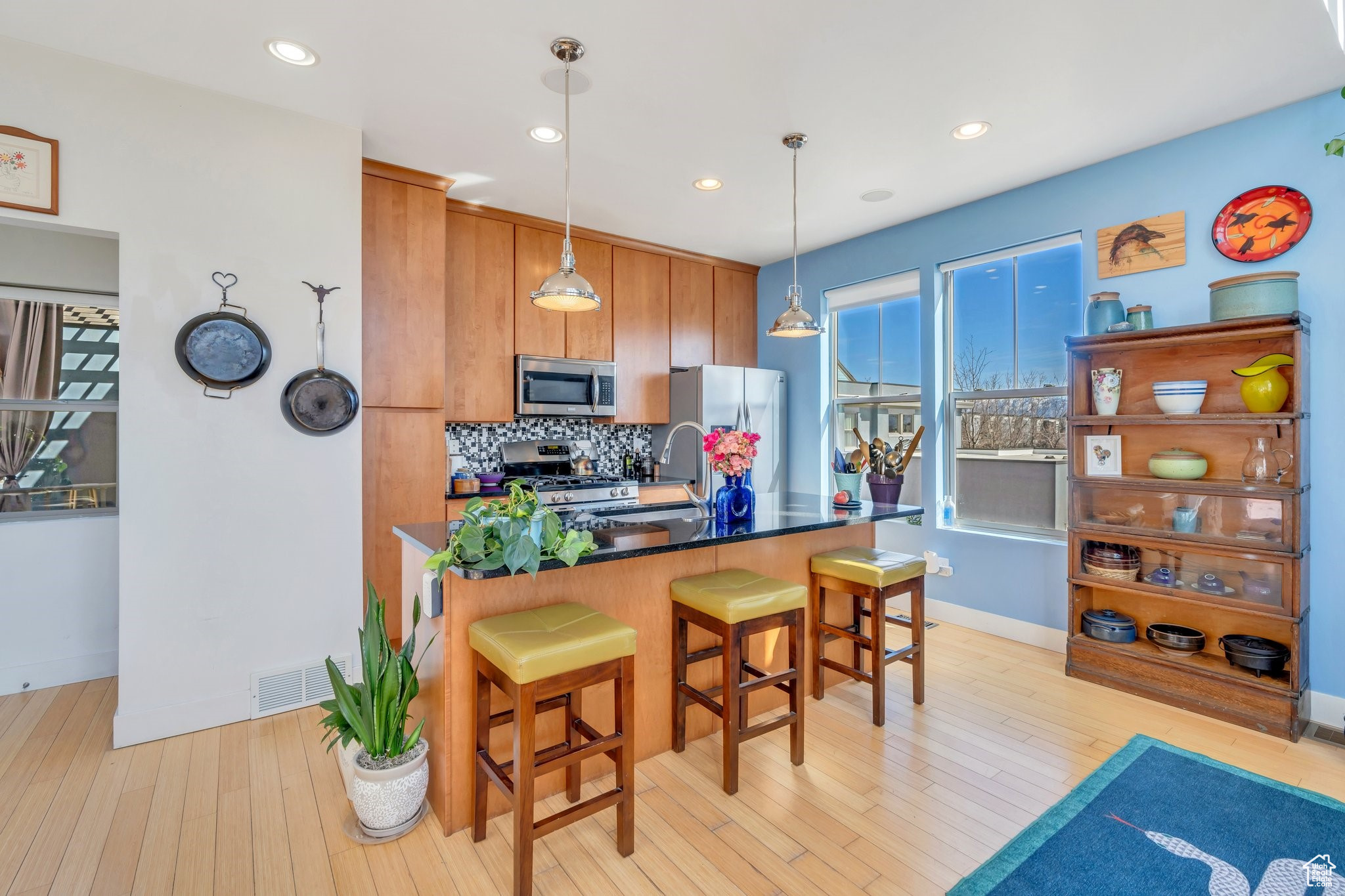 Kitchen featuring light wood finished floors, visible vents, backsplash, a kitchen bar, and stainless steel appliances