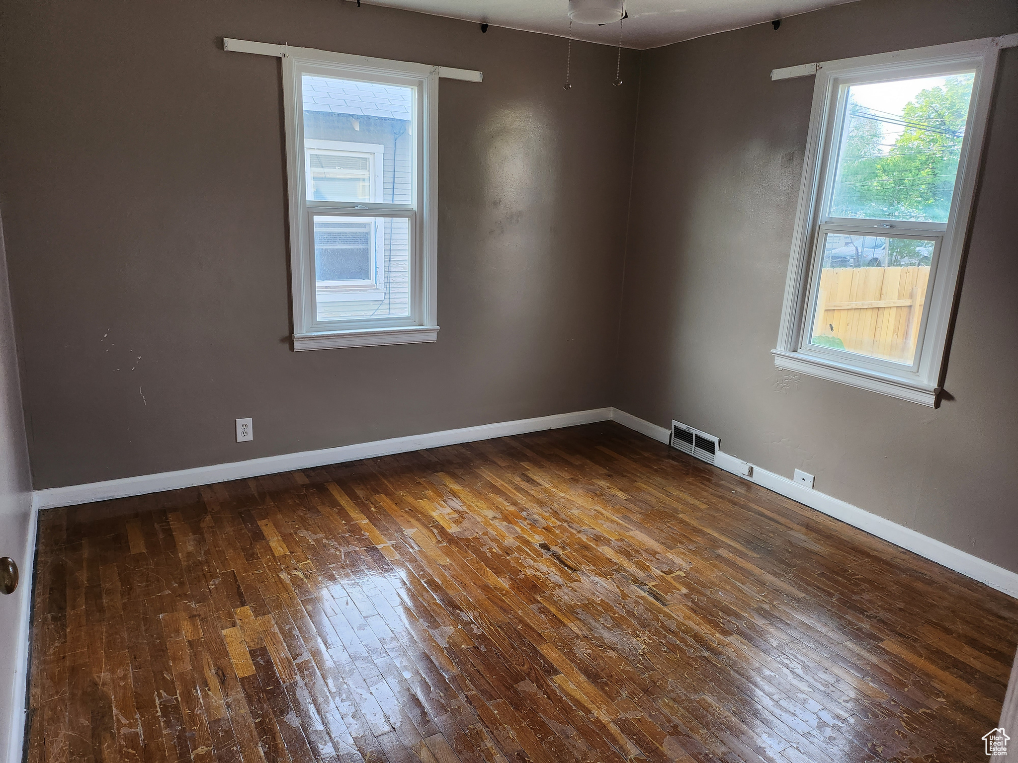 Unfurnished room with visible vents, baseboards, and dark wood-style flooring