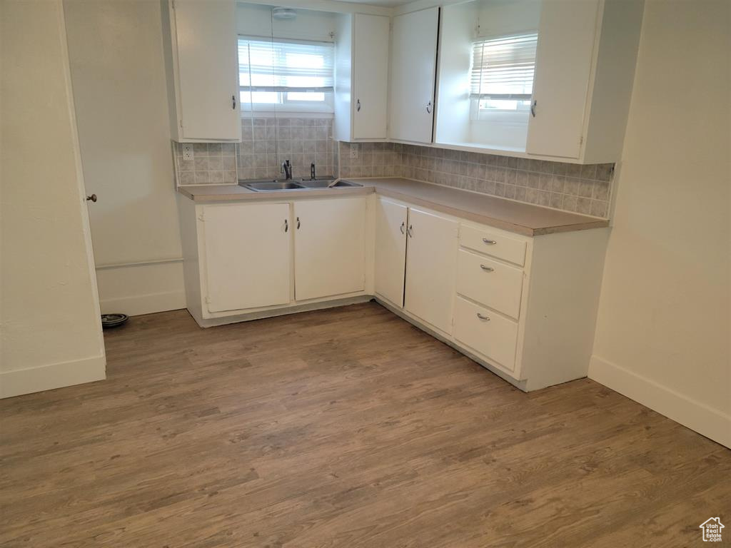 Kitchen featuring a sink, white cabinetry, backsplash, and light wood finished floors