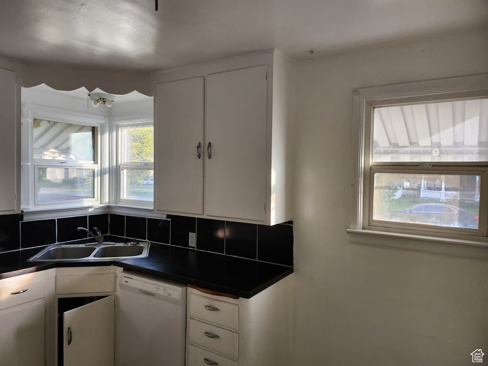 Kitchen with a sink, backsplash, dark countertops, white cabinets, and white dishwasher