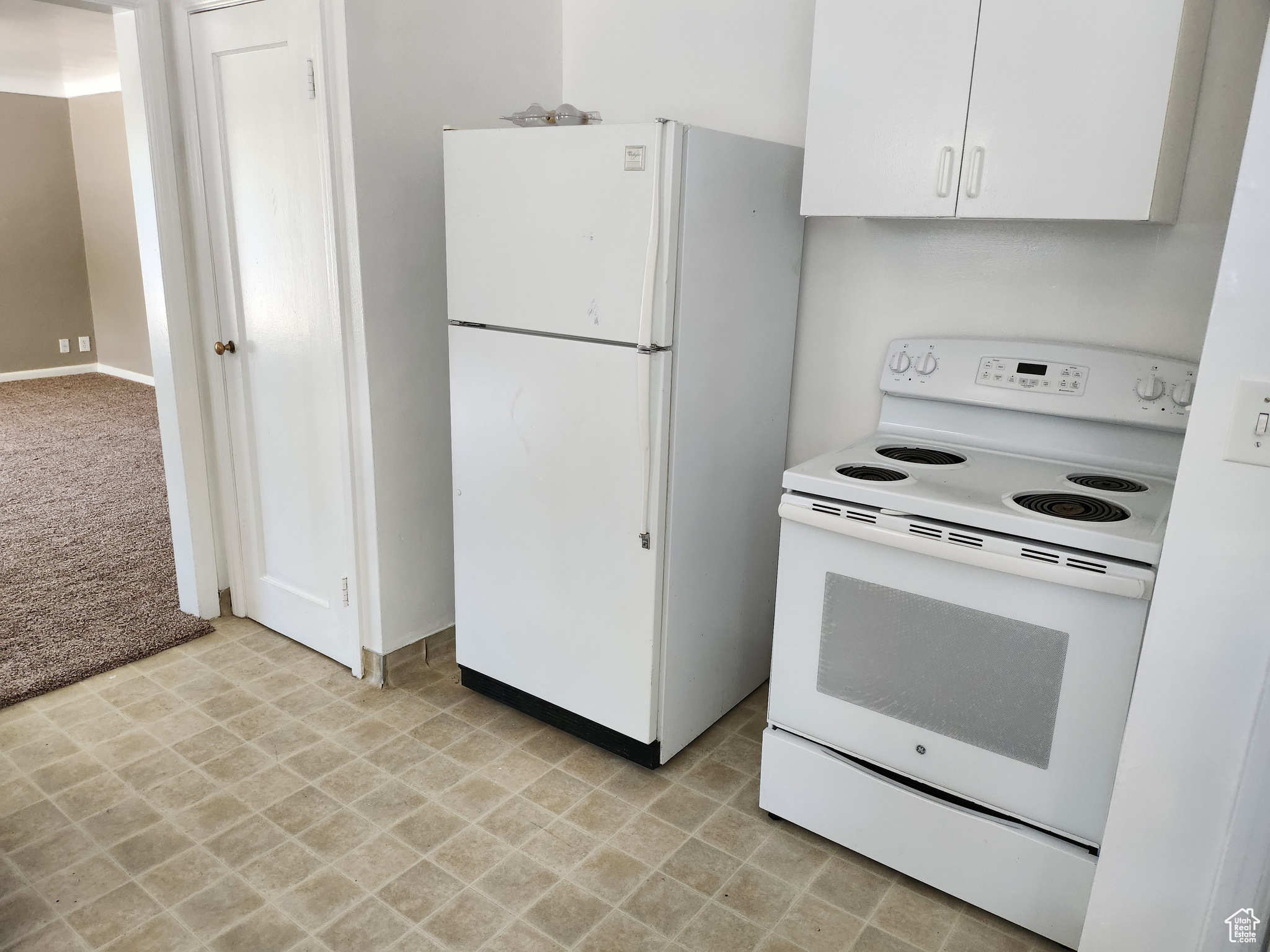 Kitchen featuring white cabinetry, white appliances, and light carpet