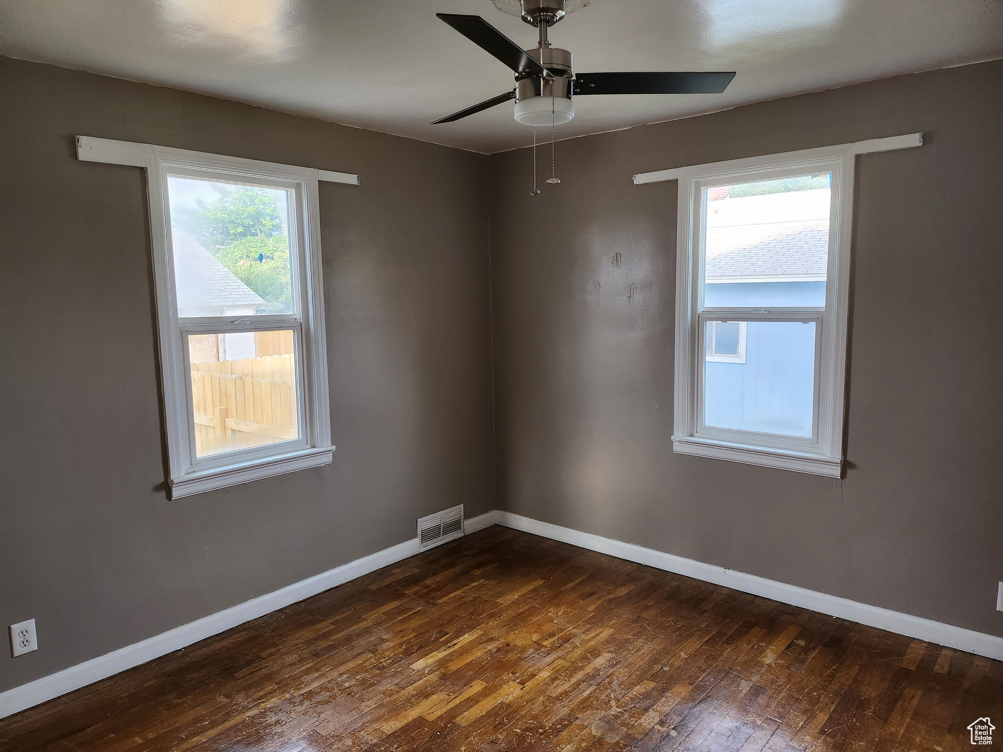 Empty room with a wealth of natural light, visible vents, baseboards, and dark wood finished floors