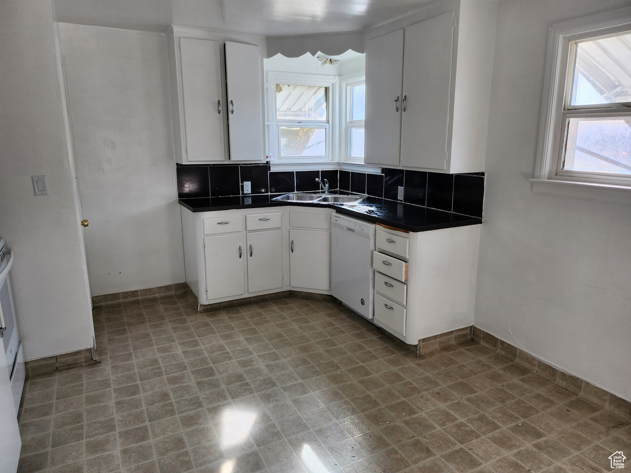 Kitchen with dark countertops, dishwasher, decorative backsplash, white cabinets, and a sink