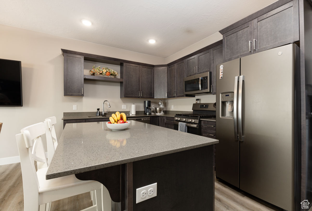 Kitchen featuring open shelves, appliances with stainless steel finishes, light wood finished floors, light stone countertops, and dark brown cabinets