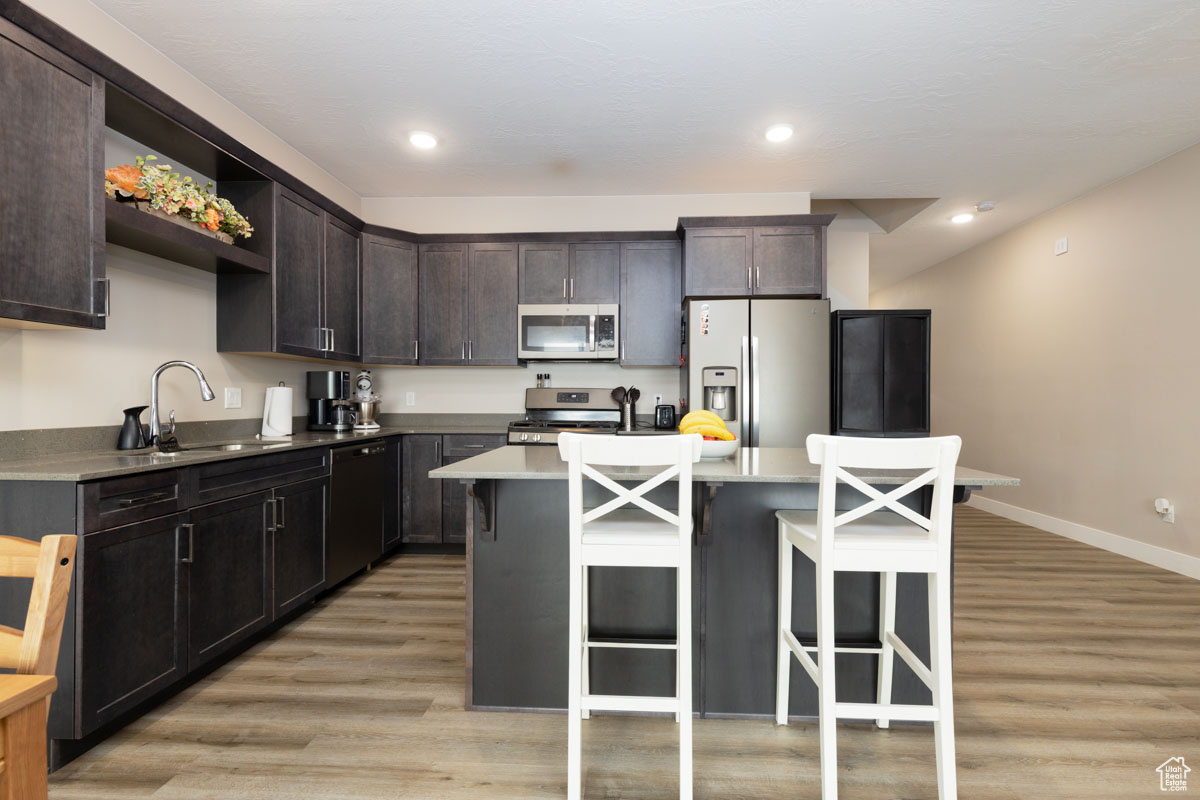 Kitchen featuring a breakfast bar area, light wood finished floors, a sink, stainless steel appliances, and a center island