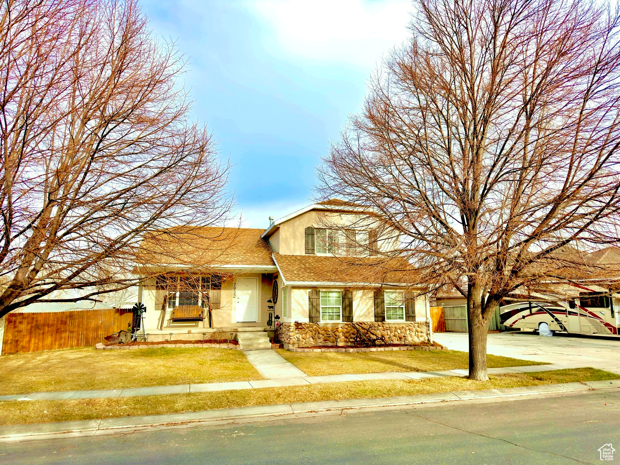 Traditional-style house featuring a front yard, fence, a shingled roof, stucco siding, and stone siding