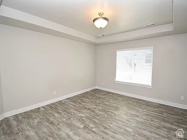 Unfurnished room with visible vents, baseboards, a tray ceiling, and dark wood-style flooring