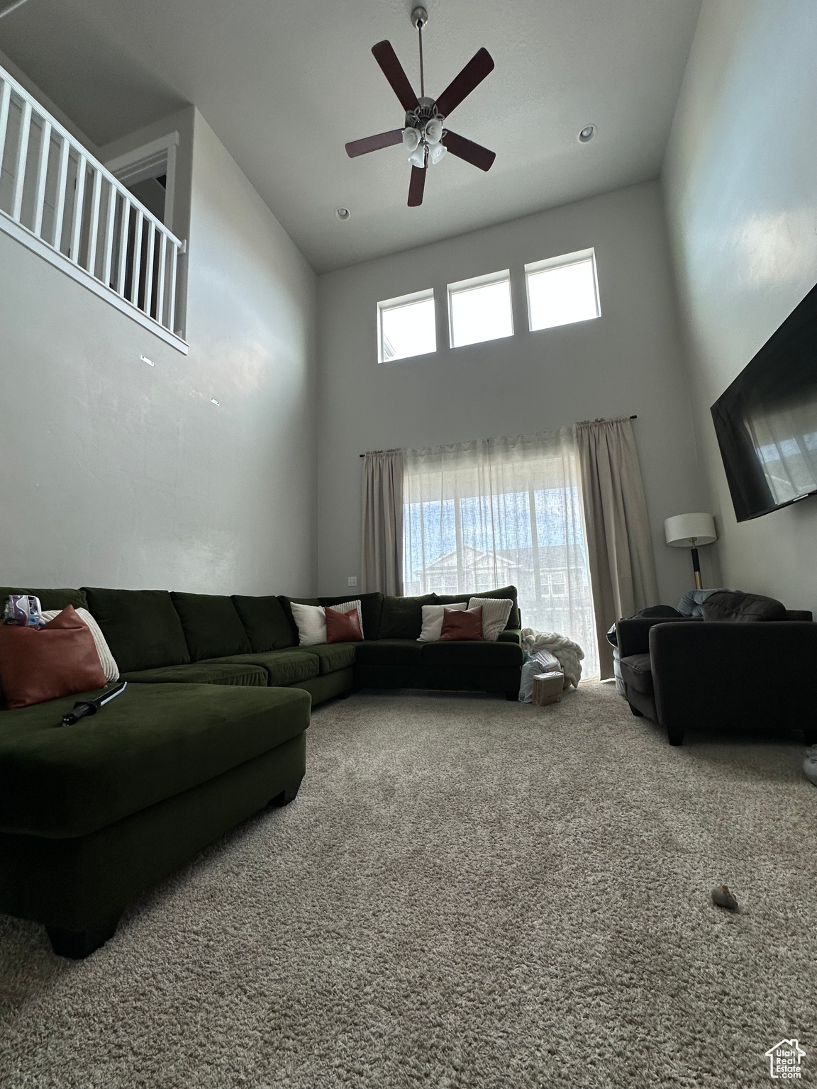 Living room featuring carpet flooring, a high ceiling, and a ceiling fan