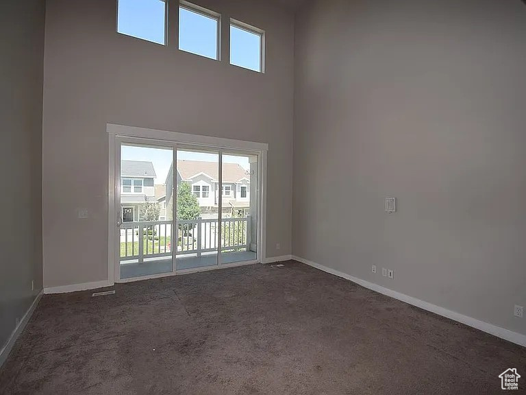 Empty room with a towering ceiling, baseboards, and dark colored carpet