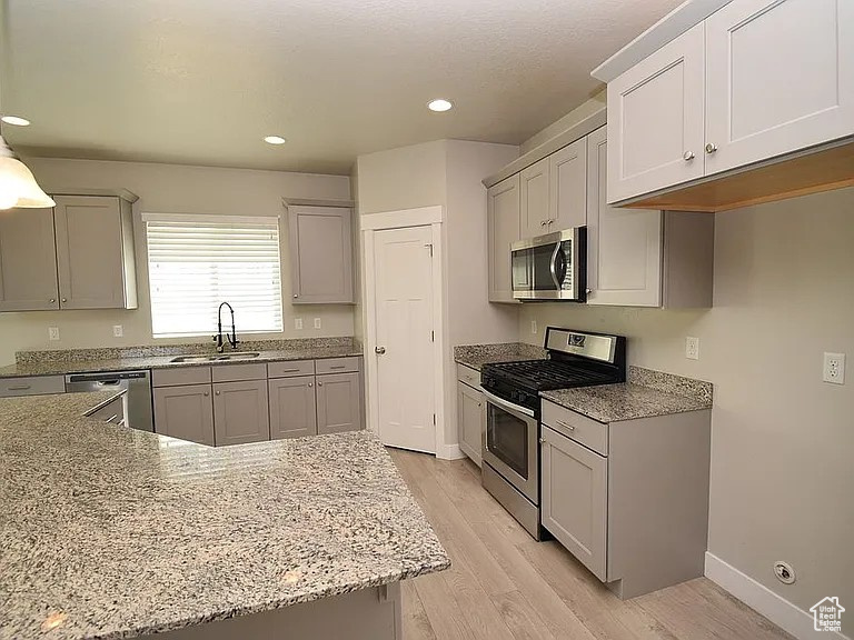 Kitchen with a sink, light stone counters, light wood-type flooring, and stainless steel appliances