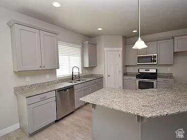 Kitchen with light stone counters, gray cabinets, appliances with stainless steel finishes, and a sink