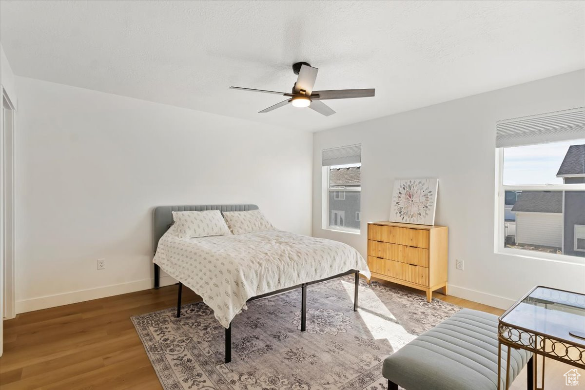 Bedroom featuring multiple windows, baseboards, light wood-type flooring, and ceiling fan