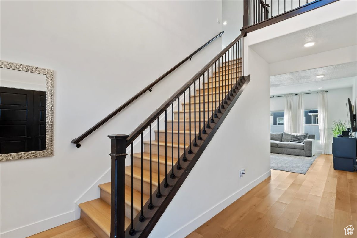 Staircase with recessed lighting, a high ceiling, baseboards, and wood finished floors