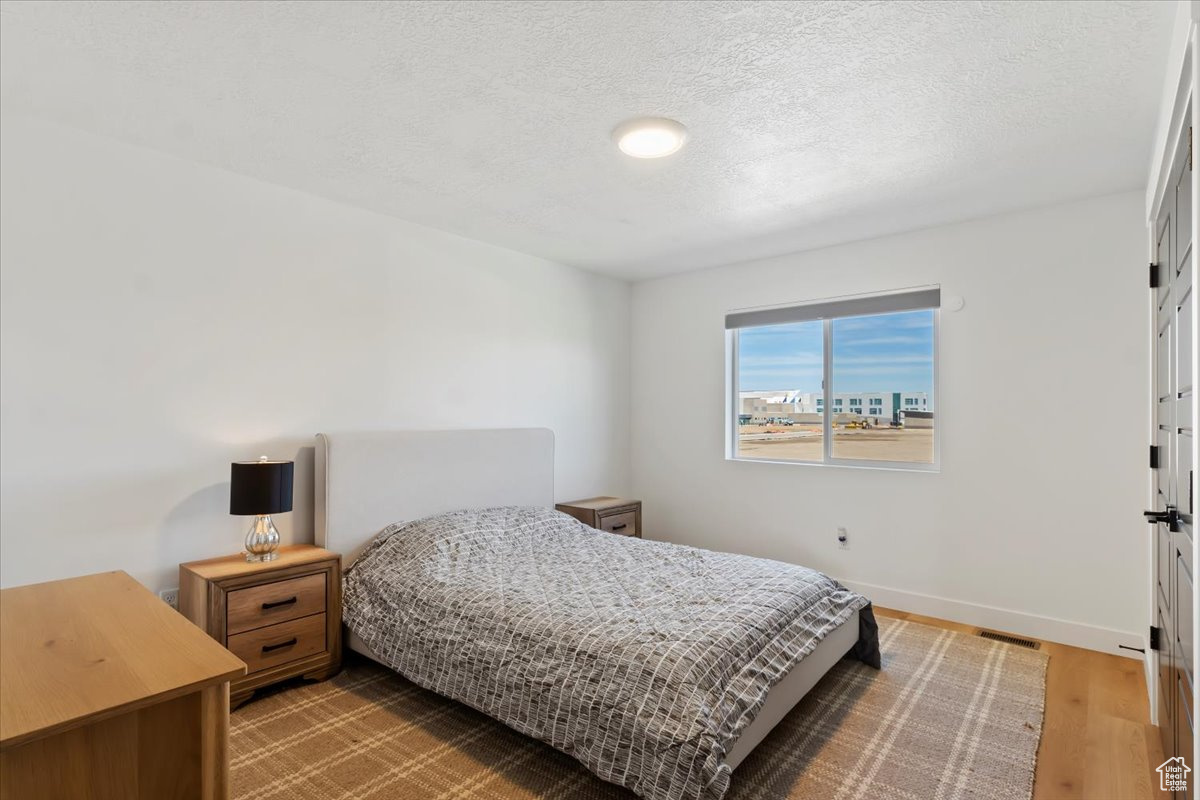 Bedroom featuring visible vents, a textured ceiling, baseboards, and wood finished floors