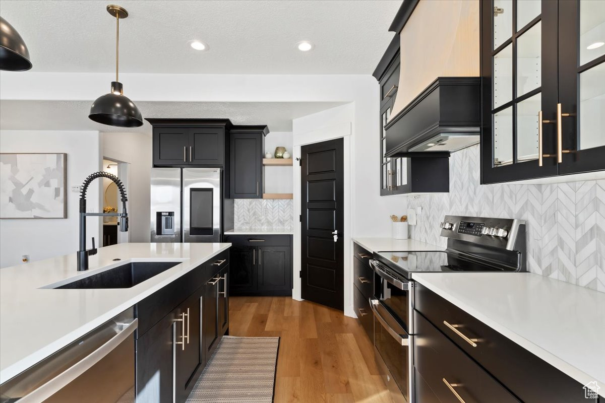 Kitchen featuring stainless steel appliances, light countertops, custom range hood, and a sink