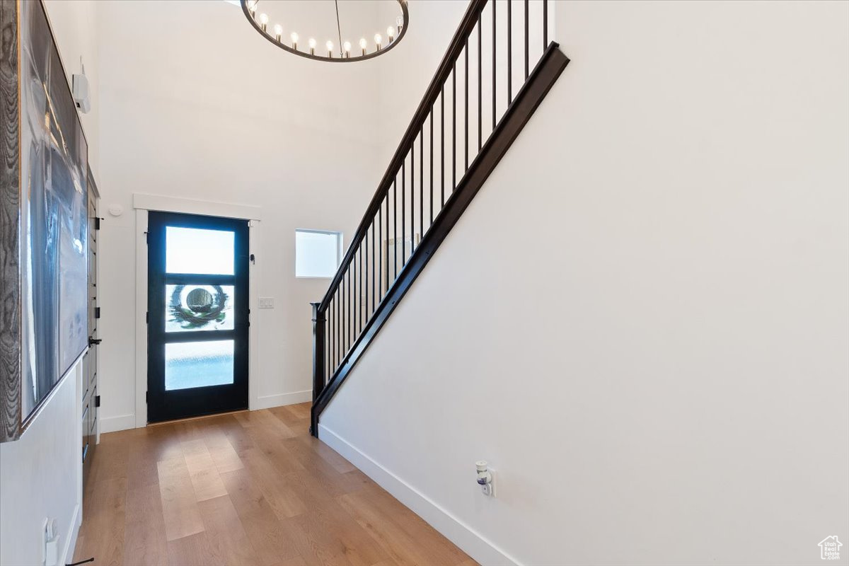 Foyer entrance with baseboards, stairs, light wood-type flooring, a high ceiling, and a notable chandelier