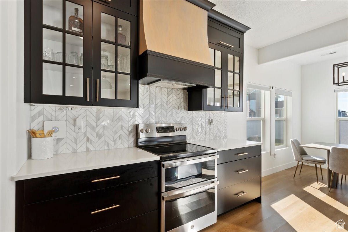 Kitchen with premium range hood, double oven range, tasteful backsplash, and light countertops