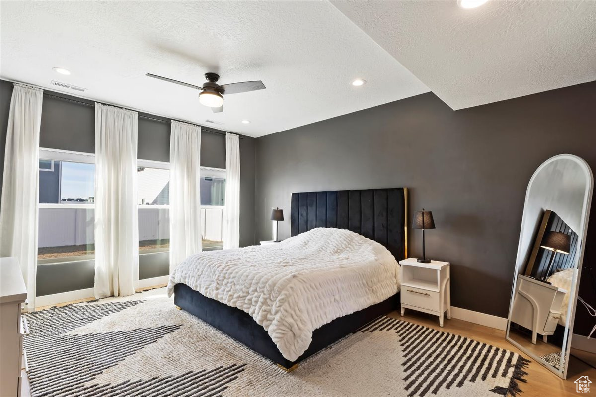 Bedroom with visible vents, ceiling fan, baseboards, wood finished floors, and a textured ceiling