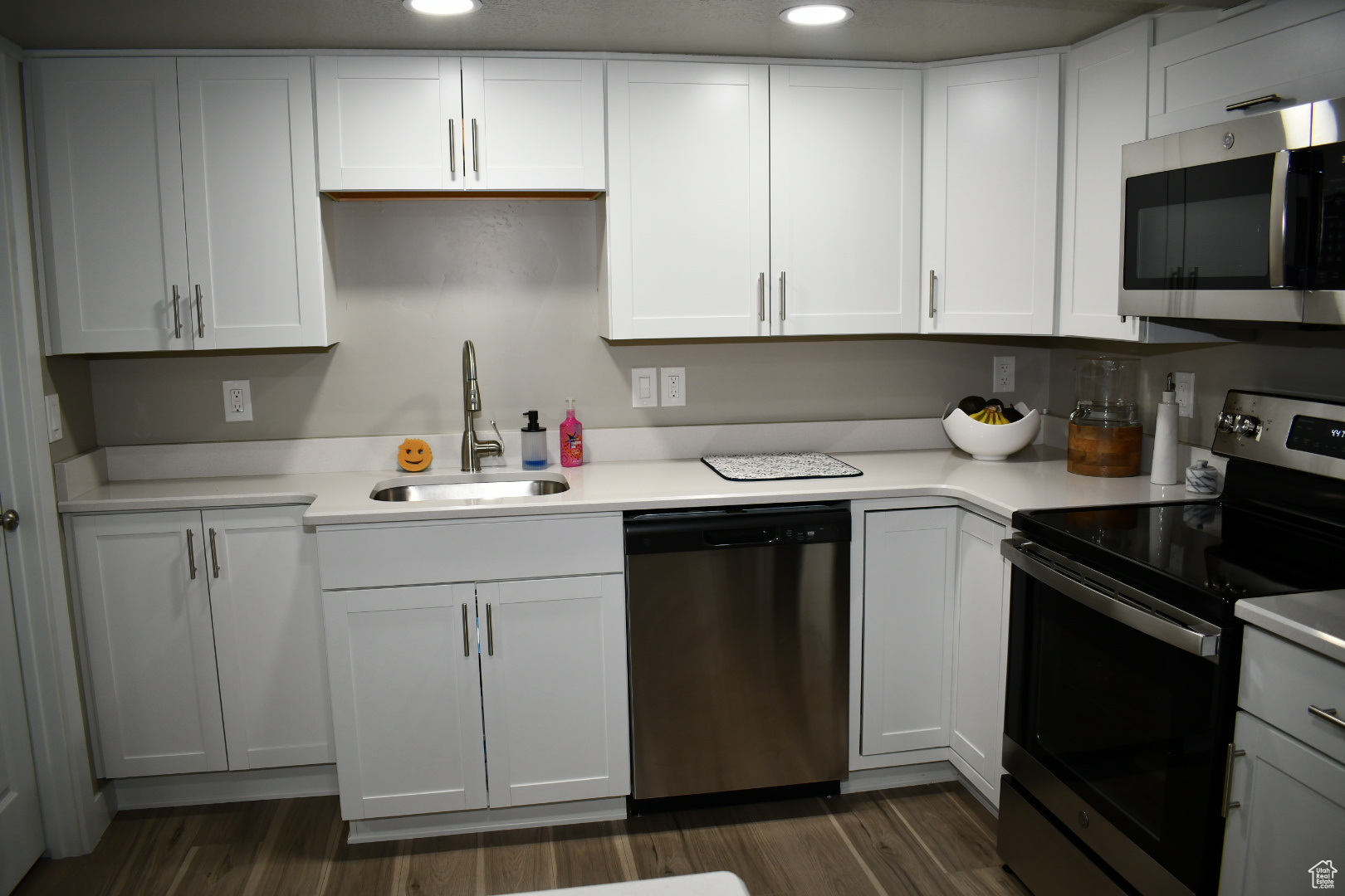 Kitchen featuring stainless steel appliances, light countertops, a sink, and dark wood-style floors