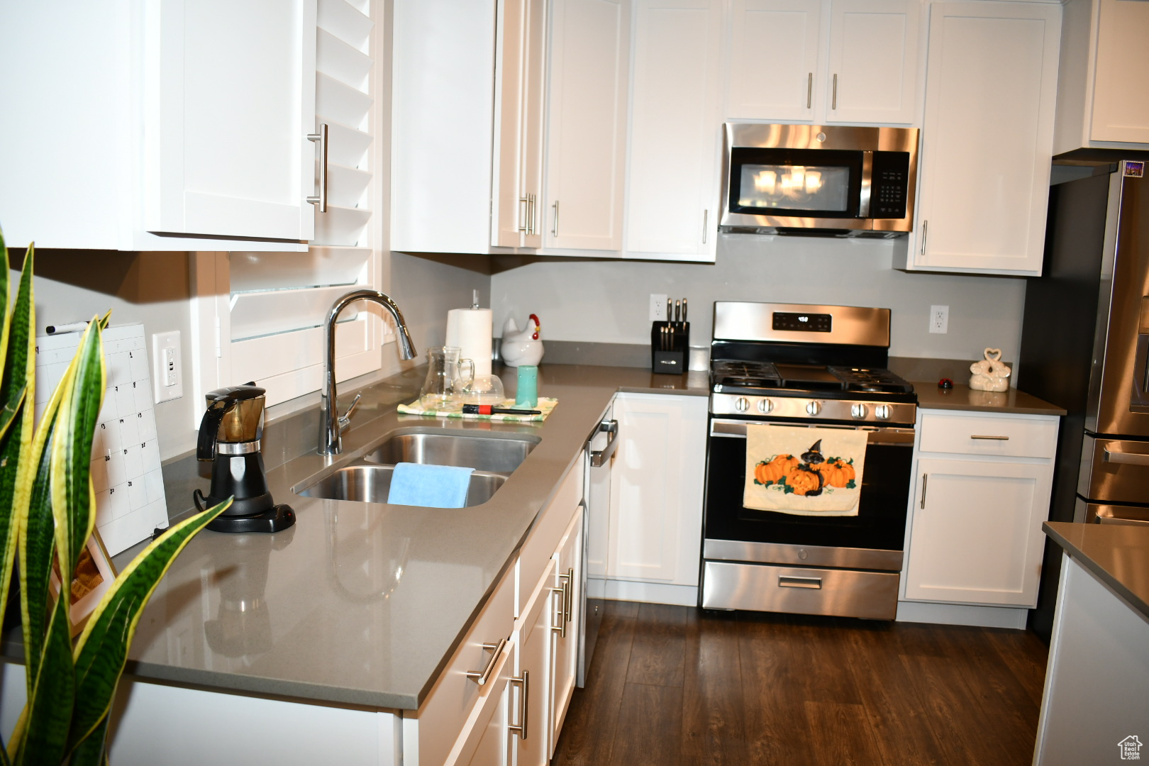 Kitchen with dark wood-style flooring, appliances with stainless steel finishes, white cabinets, and a sink