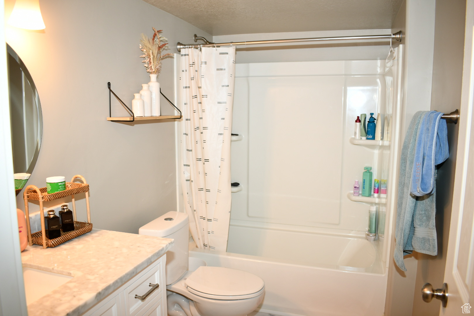 Bathroom with toilet, a textured ceiling, vanity, and shower / bath combo with shower curtain