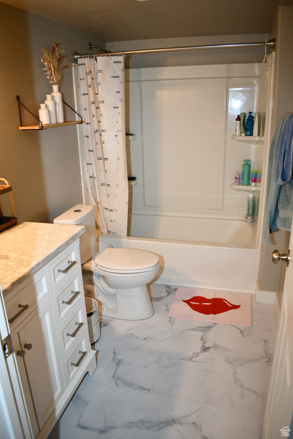Bathroom with marble finish floor, toilet, shower / tub combo, vanity, and a textured ceiling