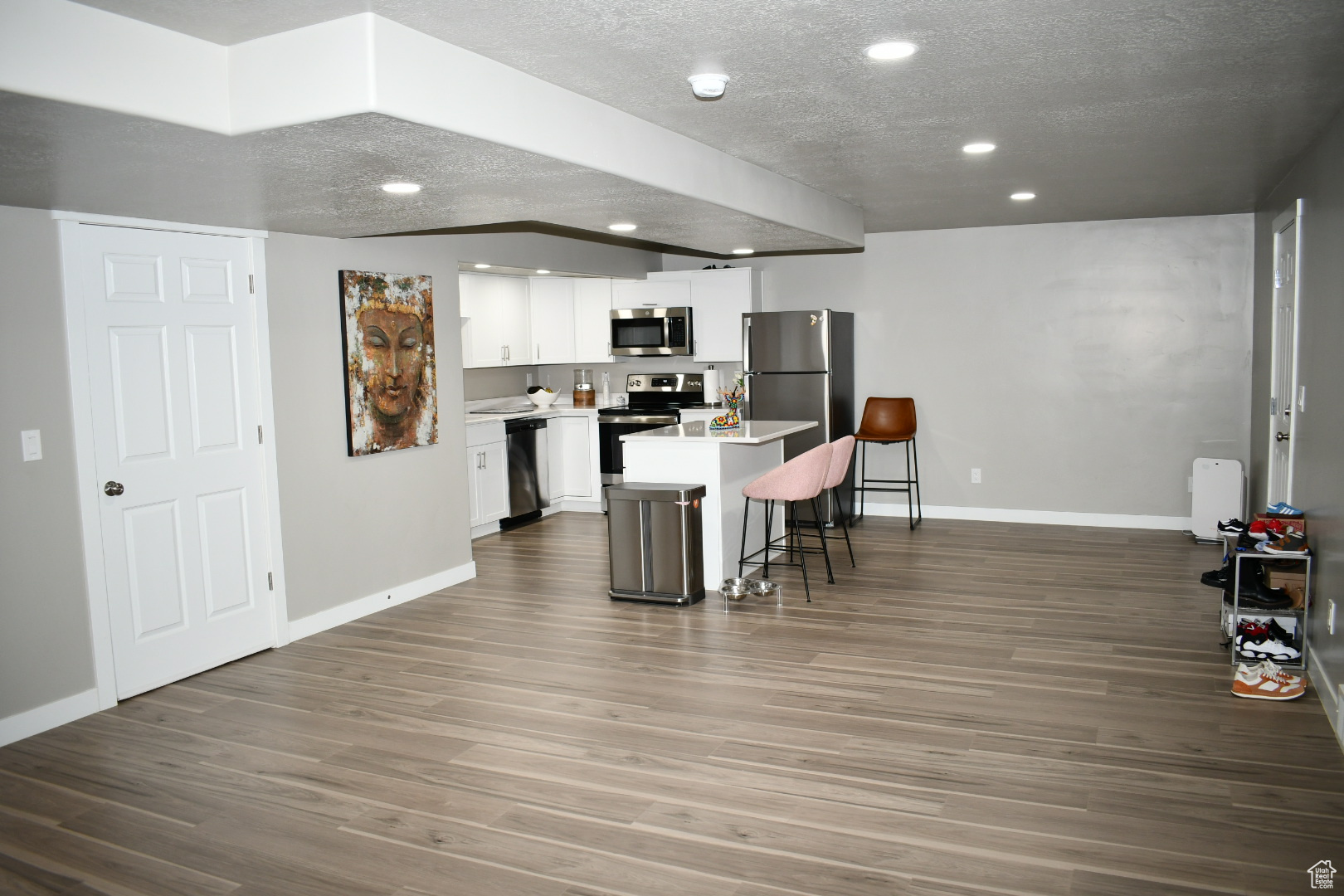 Kitchen with a textured ceiling, a breakfast bar area, wood finished floors, white cabinets, and appliances with stainless steel finishes