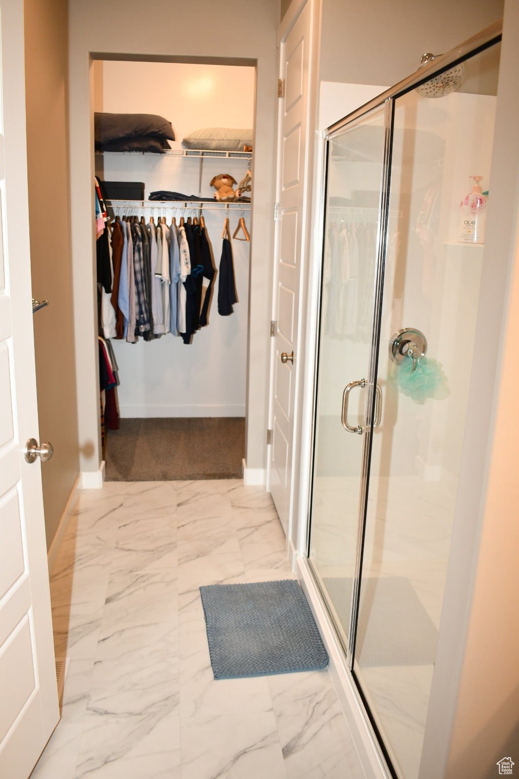 Full bathroom with marble finish floor, a shower stall, a walk in closet, and baseboards