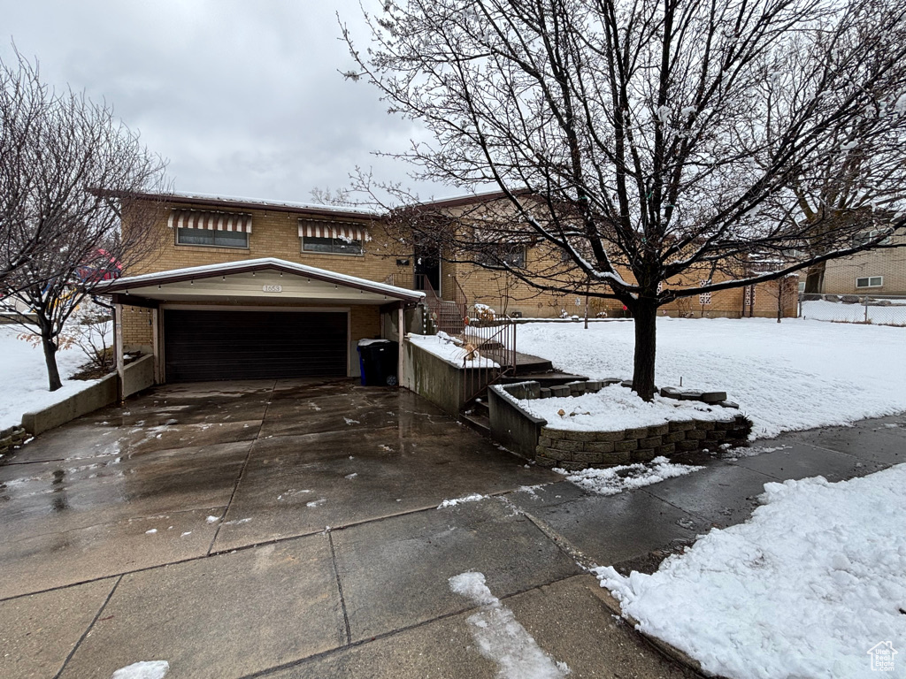 View of snowy exterior featuring a garage, brick siding, and concrete driveway