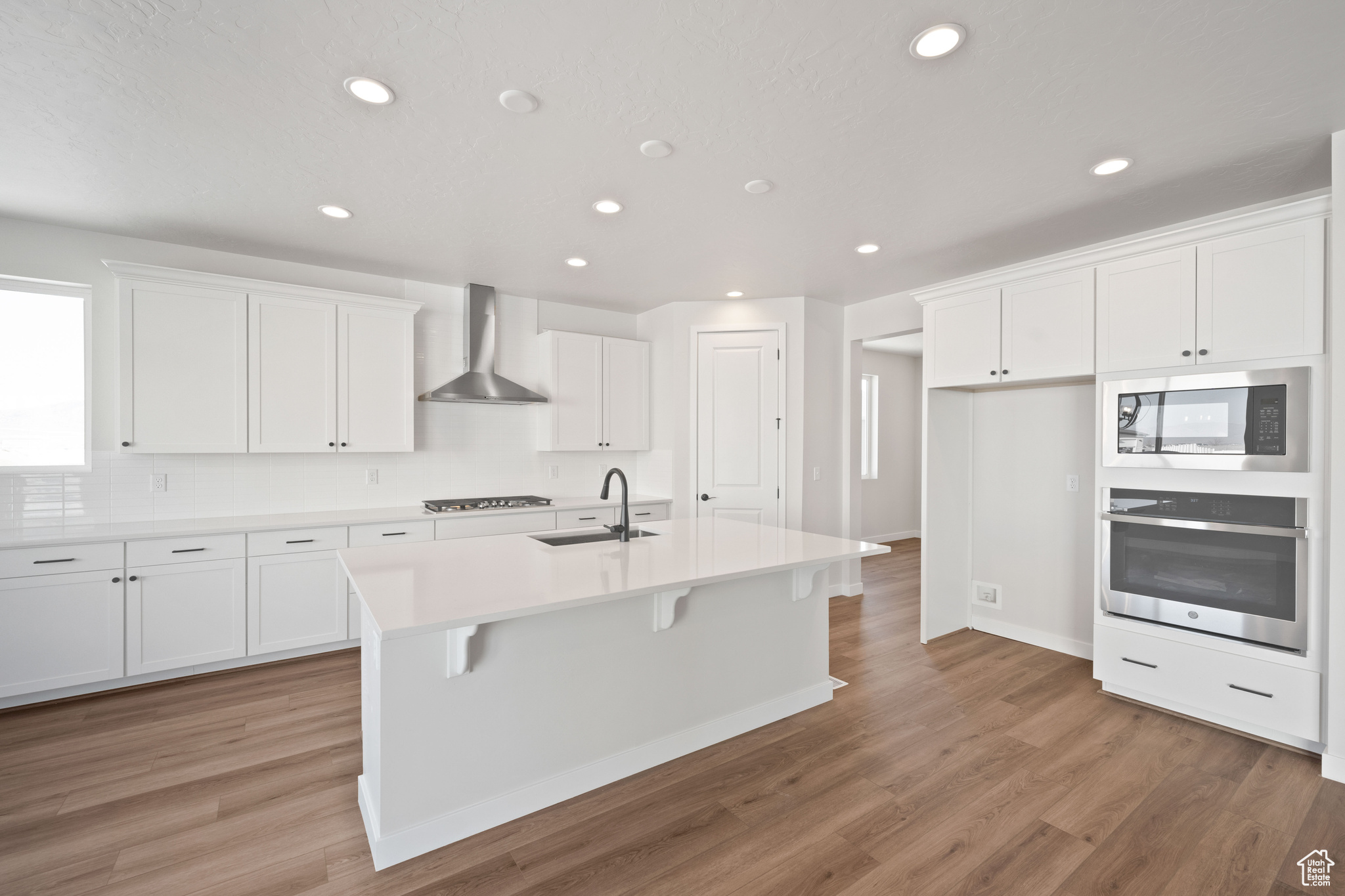 Kitchen featuring oven, built in microwave, white cabinets, wall chimney exhaust hood, and a sink