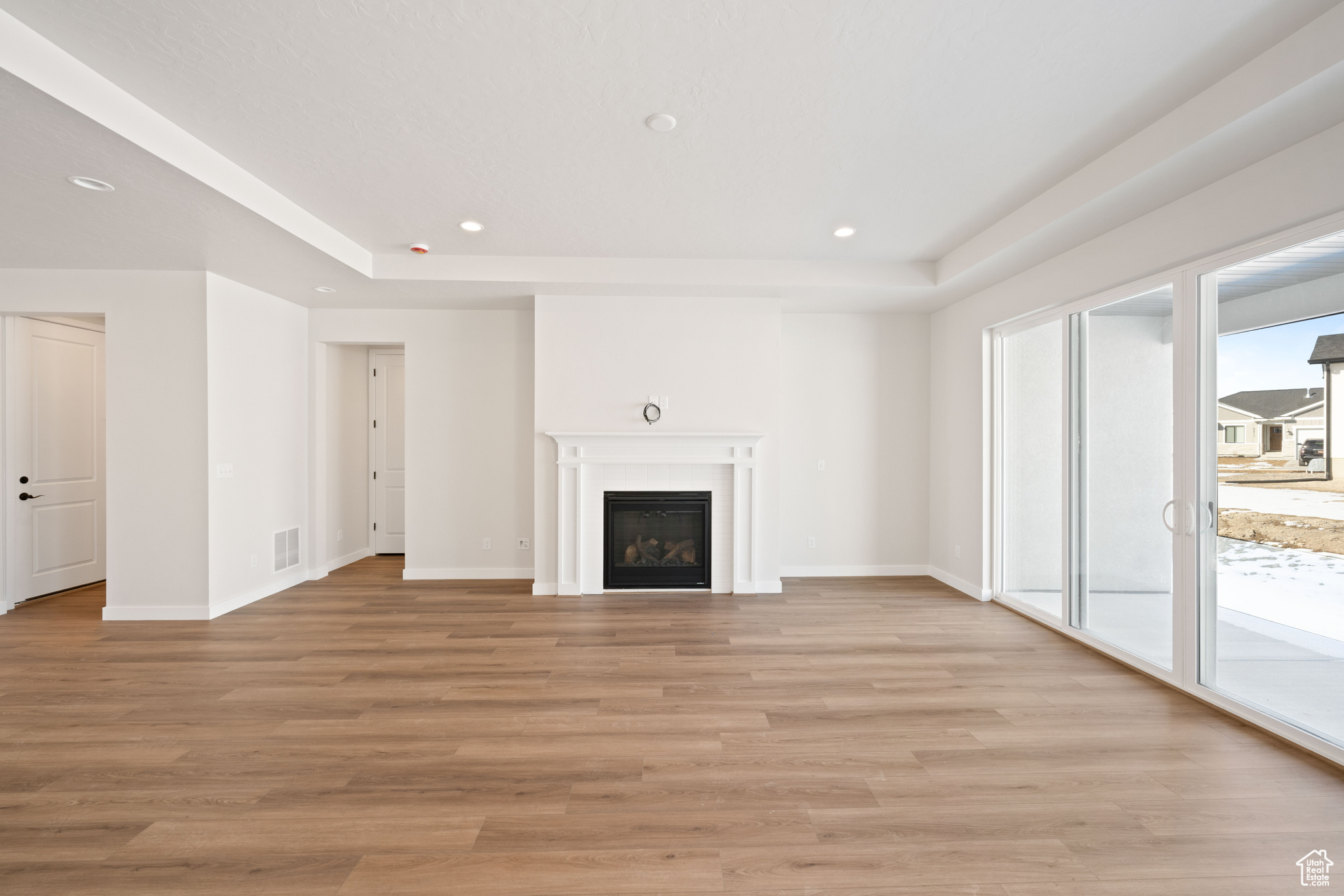 Unfurnished living room with light wood finished floors, recessed lighting, baseboards, and a tray ceiling