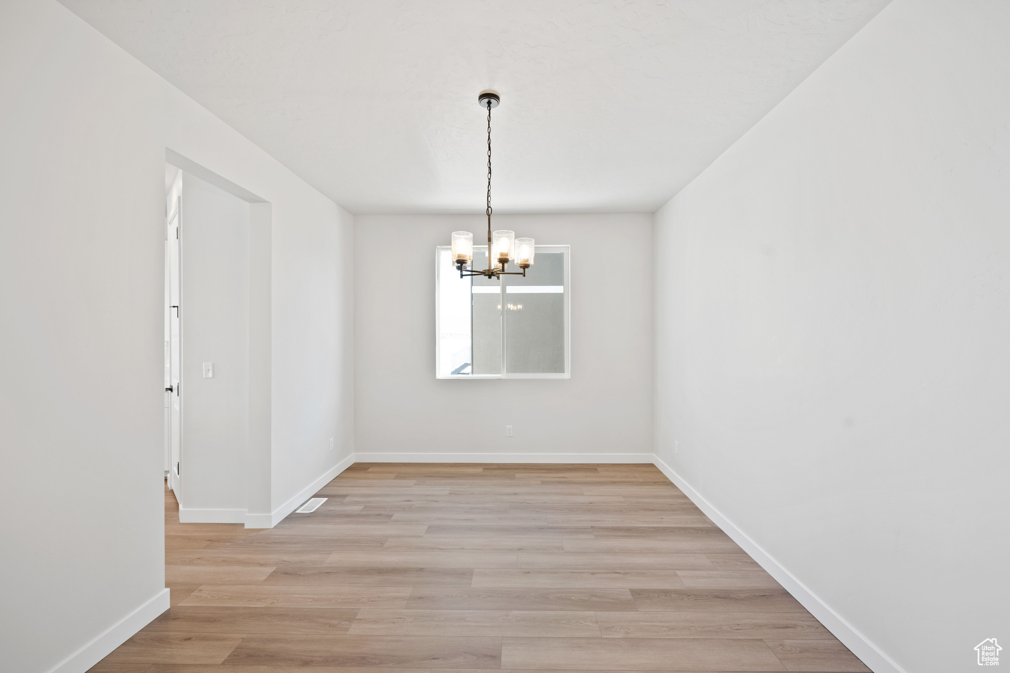 Unfurnished dining area featuring light wood-style flooring, a notable chandelier, and baseboards