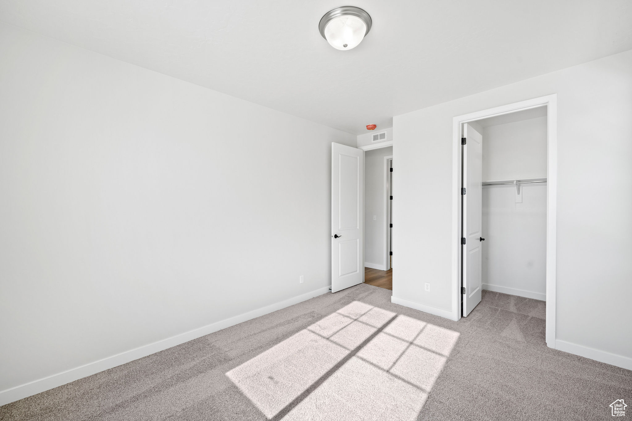 Unfurnished bedroom with baseboards, light carpet, visible vents, and a walk in closet