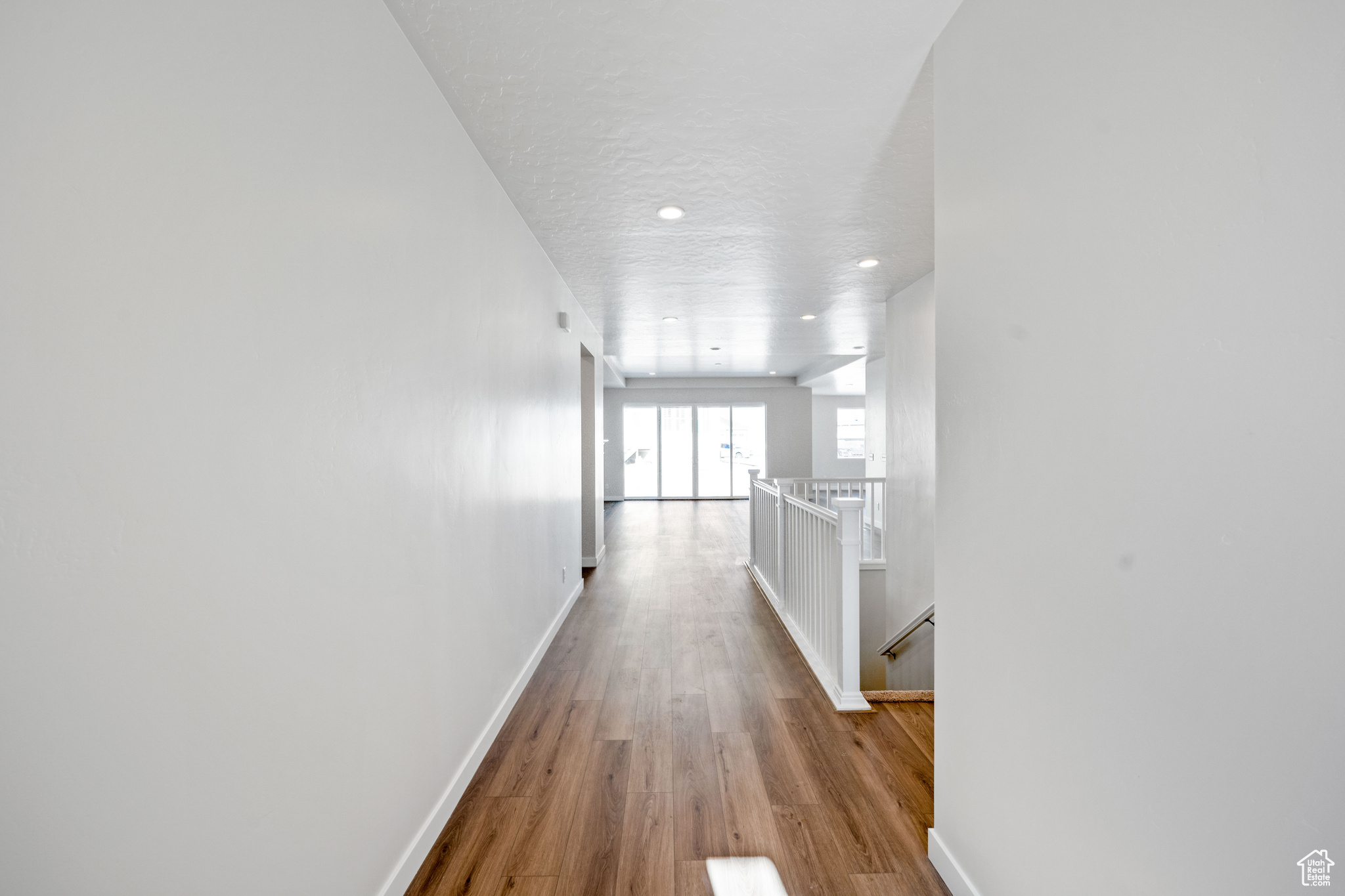 Hallway featuring wood finished floors, baseboards, recessed lighting, a textured ceiling, and an upstairs landing
