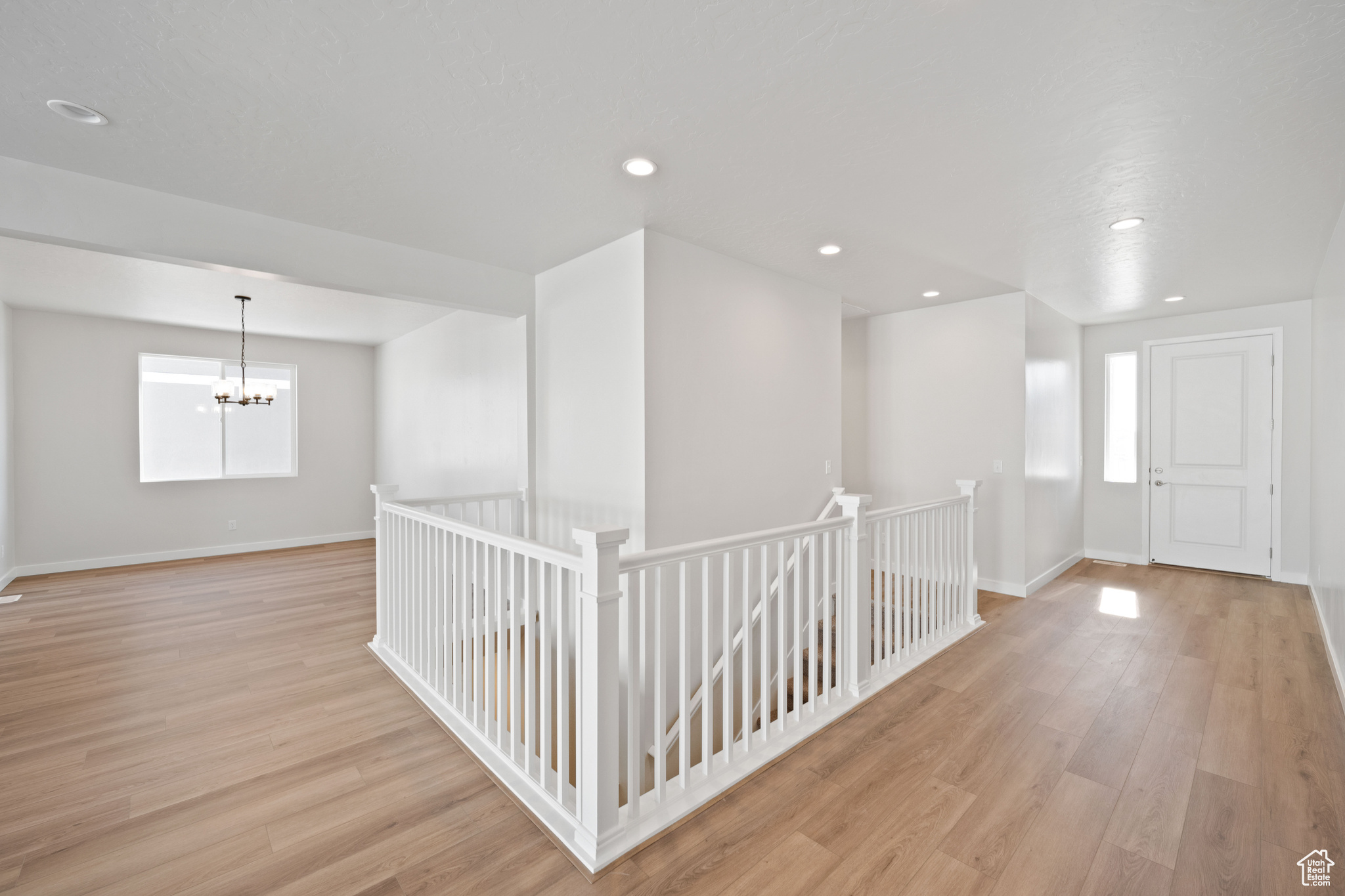 Interior space featuring light wood finished floors, baseboards, a chandelier, an upstairs landing, and recessed lighting