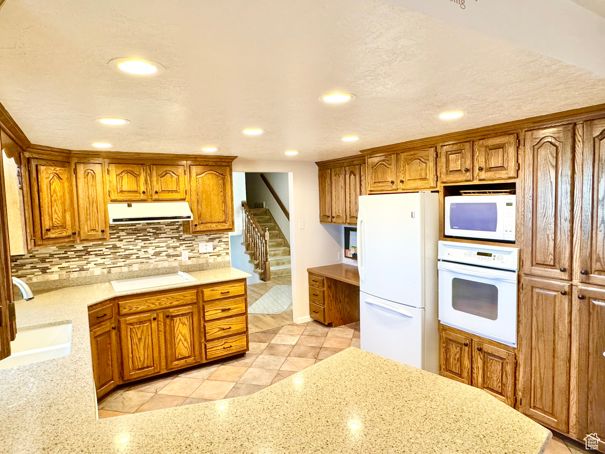 Kitchen featuring white appliances, ventilation hood, light stone counters, a sink, and decorative backsplash