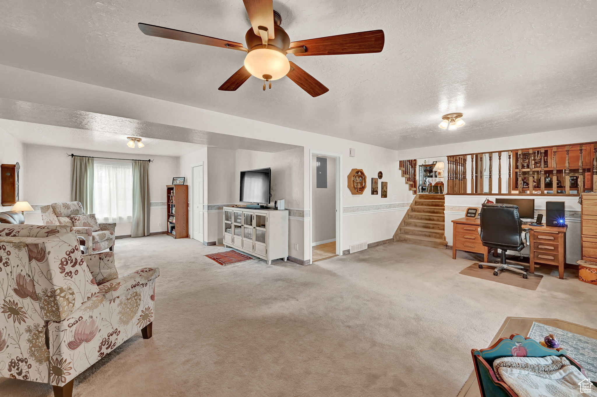 Carpeted living area featuring ceiling fan, stairway, visible vents, and a textured ceiling