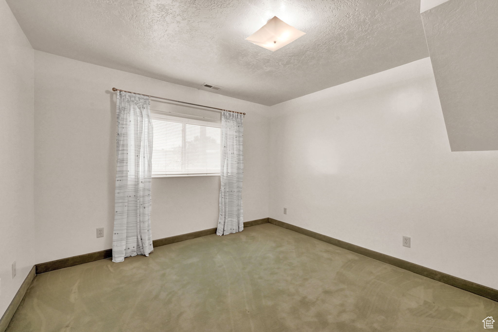 Carpeted spare room featuring visible vents, baseboards, and a textured ceiling