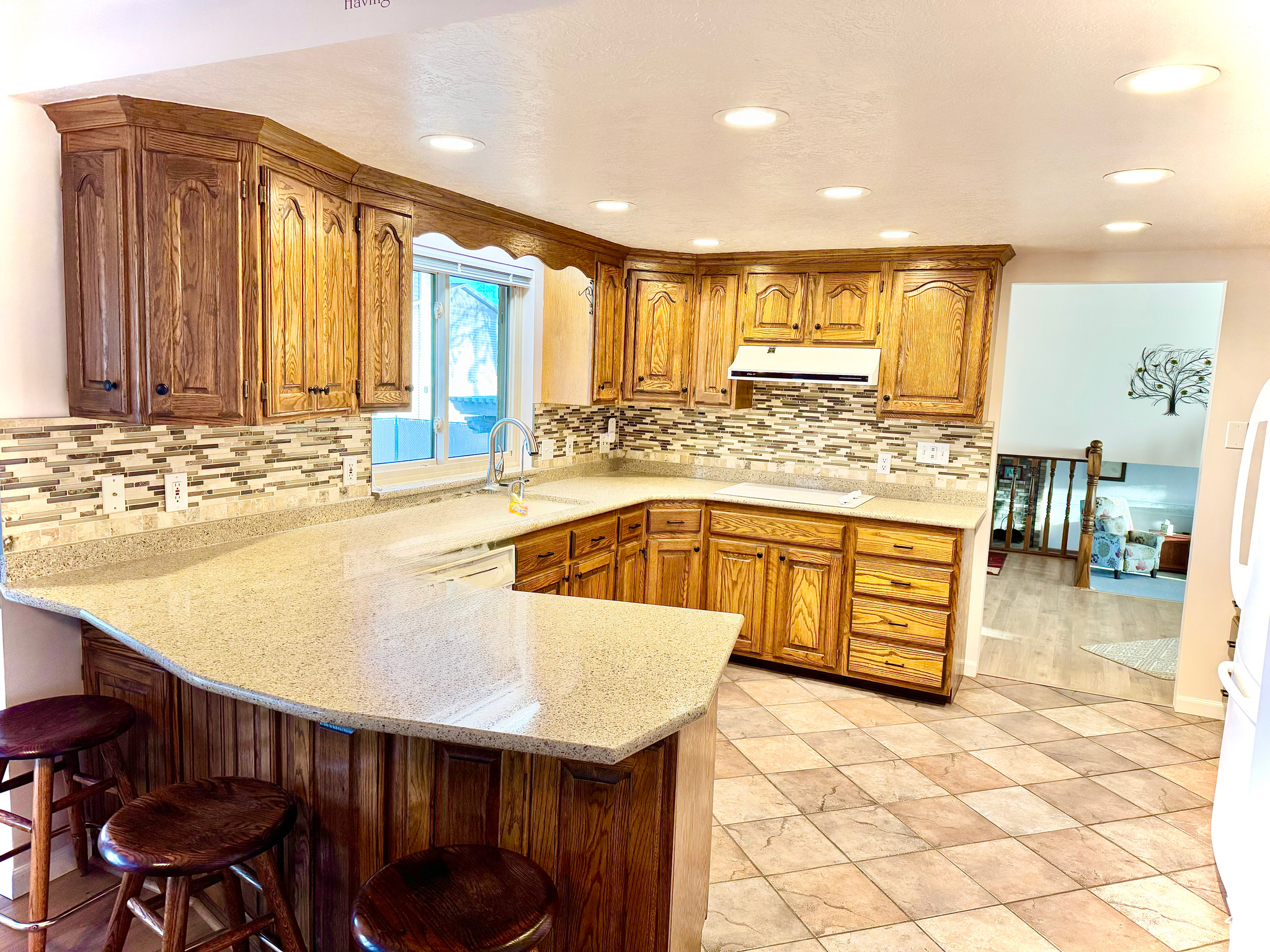 Kitchen featuring a kitchen breakfast bar, ventilation hood, a peninsula, brown cabinetry, and white cooktop
