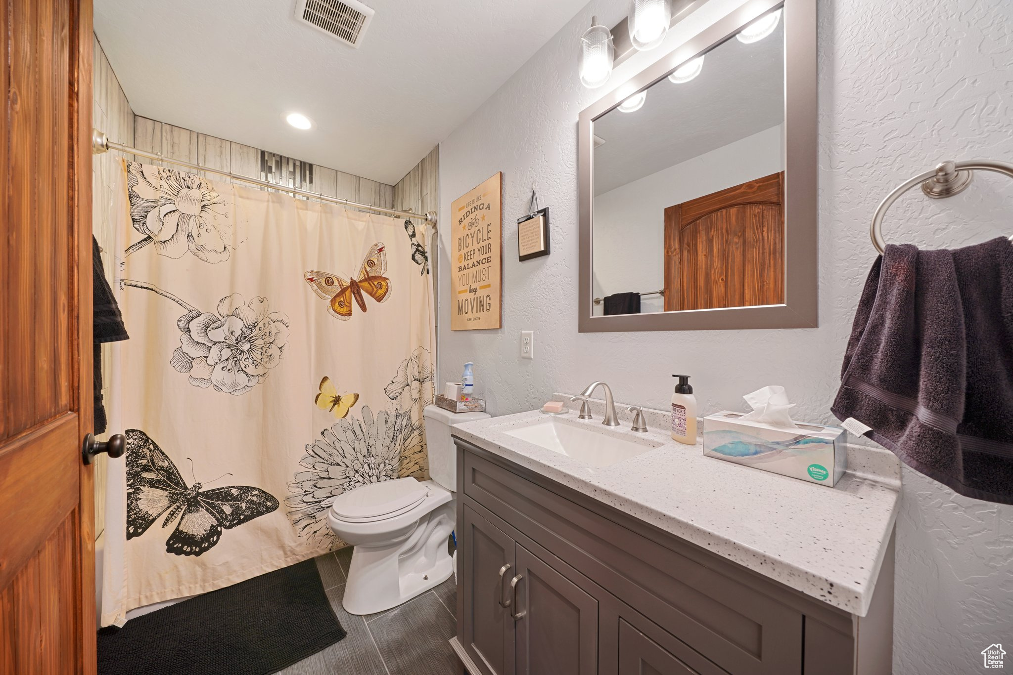 Bathroom with visible vents, toilet, a shower with shower curtain, vanity, and a textured wall