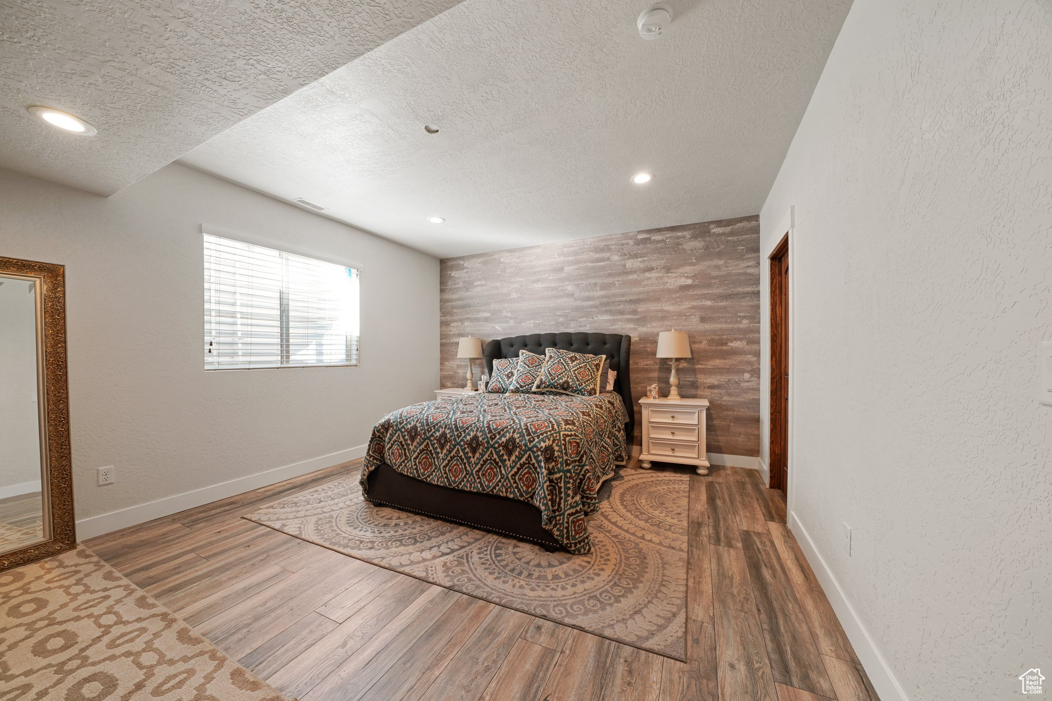 Bedroom featuring a textured ceiling, an accent wall, baseboards, and wood finished floors