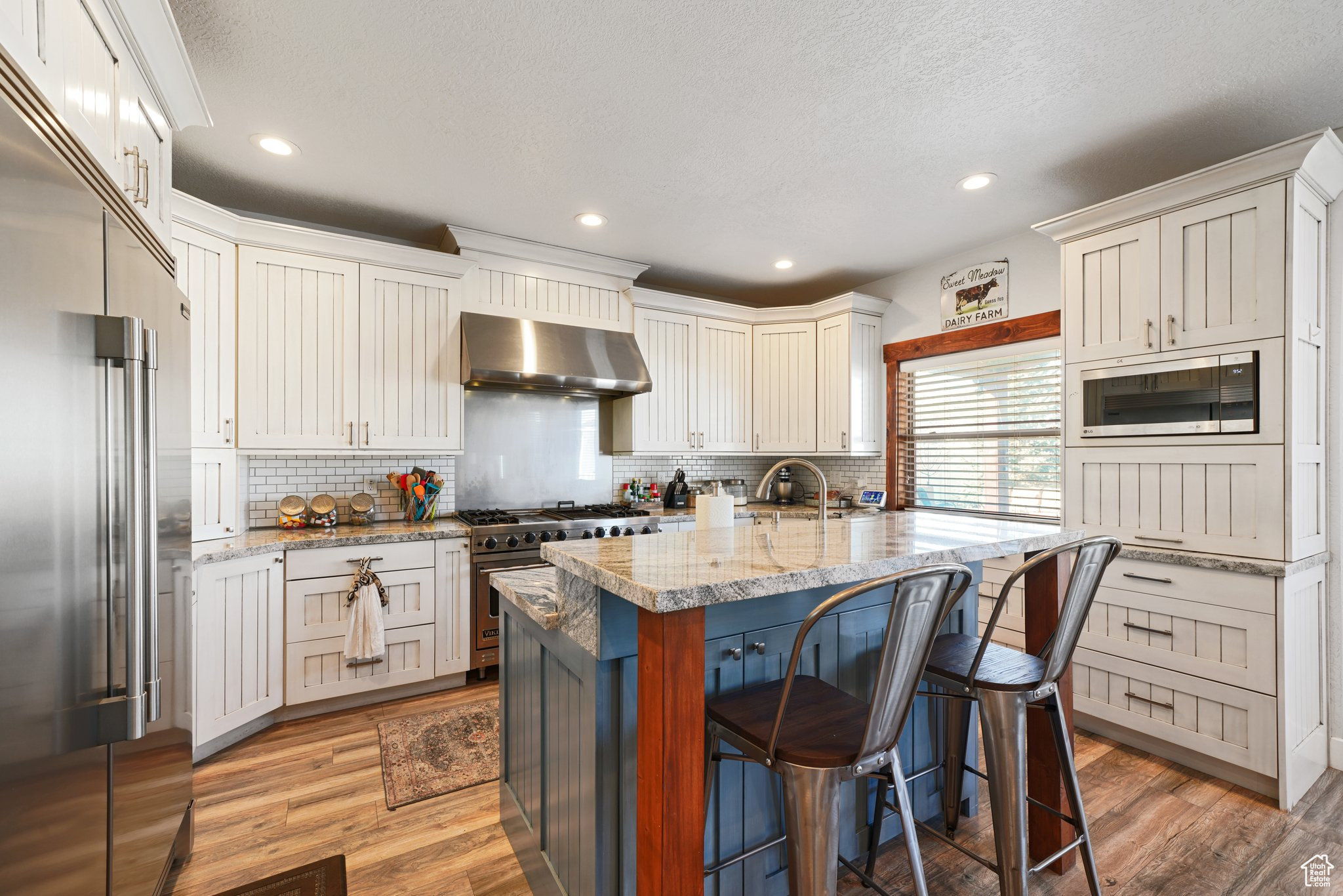 Kitchen with light wood finished floors, a breakfast bar area, wall chimney exhaust hood, and built in appliances