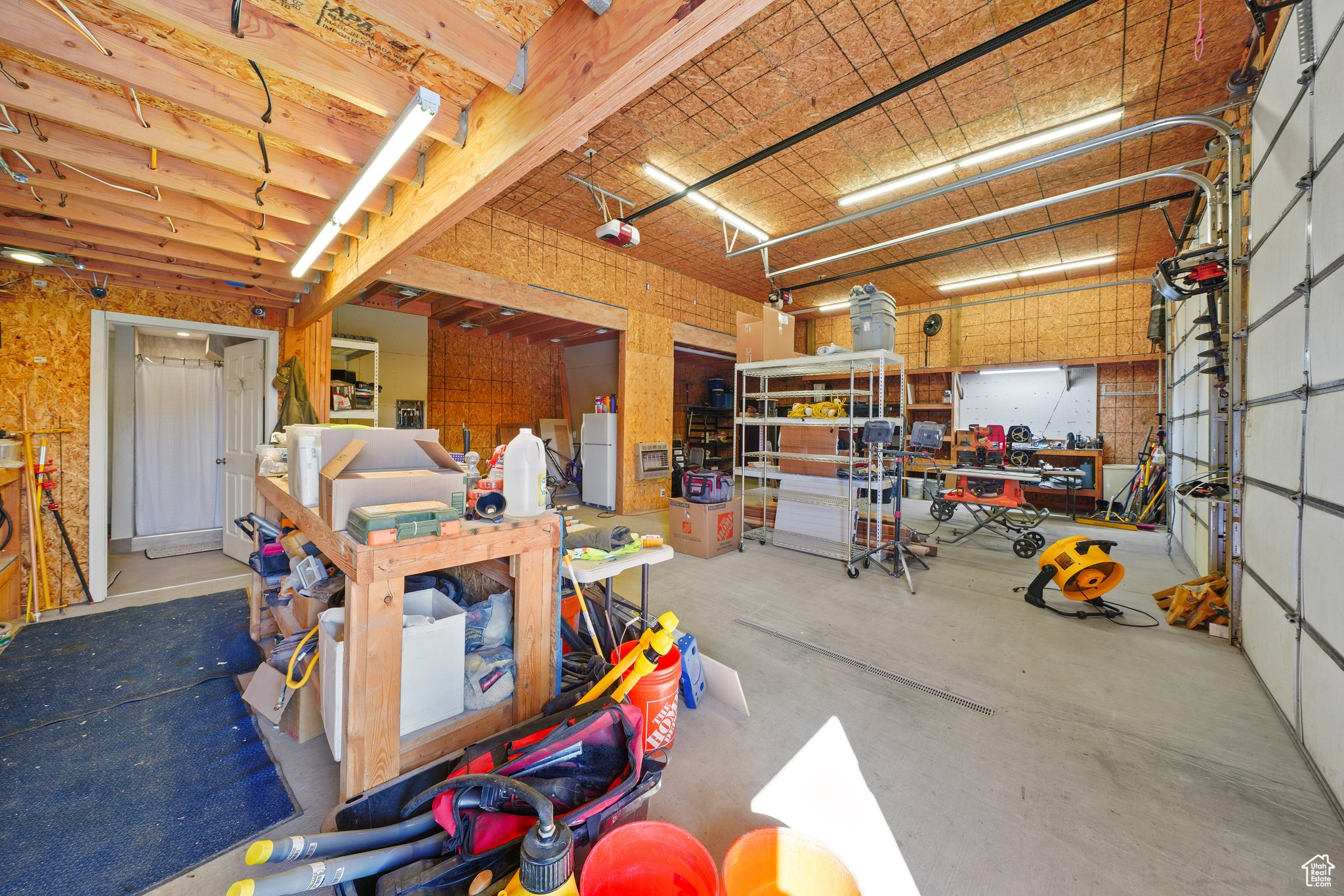 Garage featuring a workshop area, a garage door opener, and freestanding refrigerator