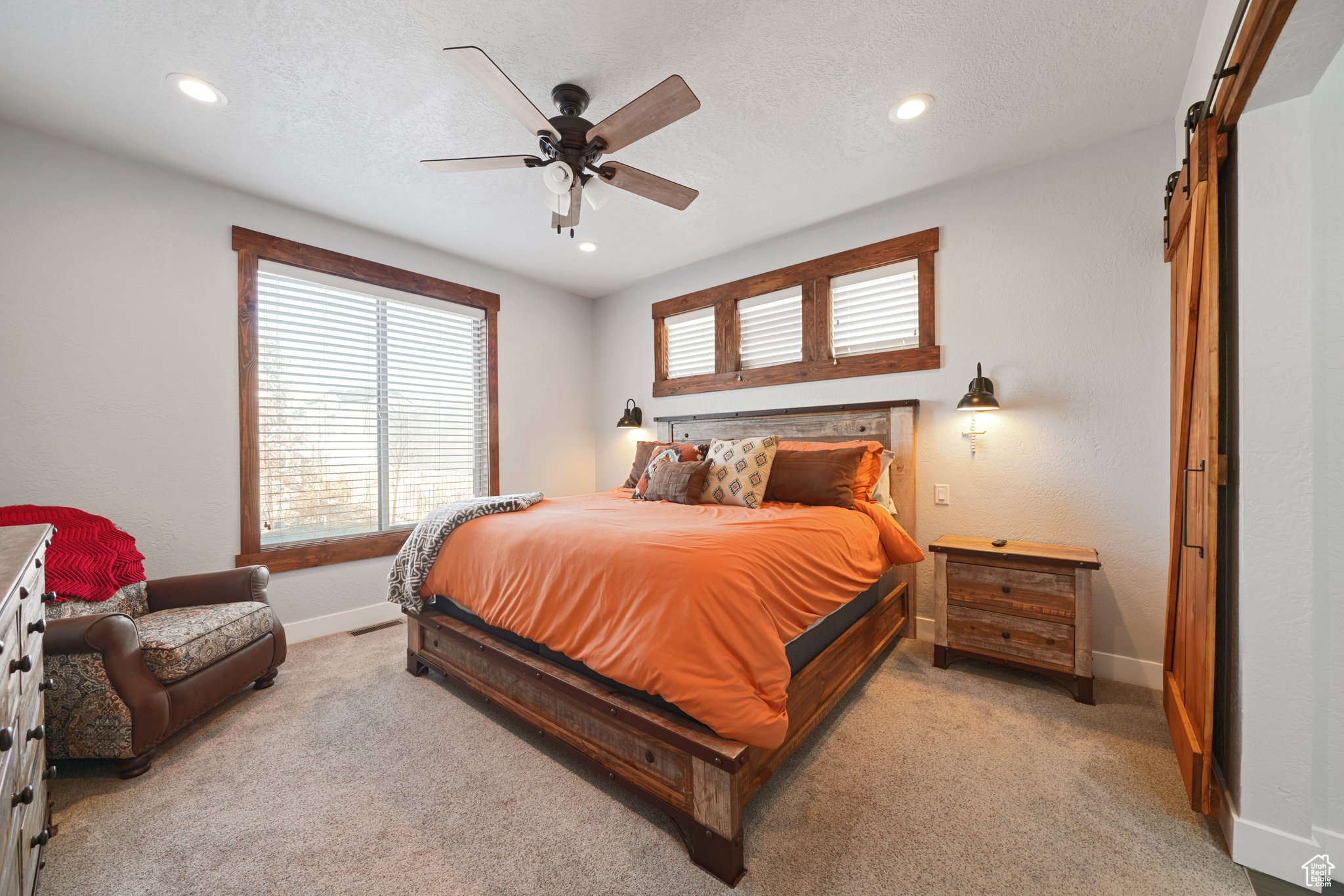 Bedroom with light colored carpet, a textured ceiling, baseboards, and a barn door