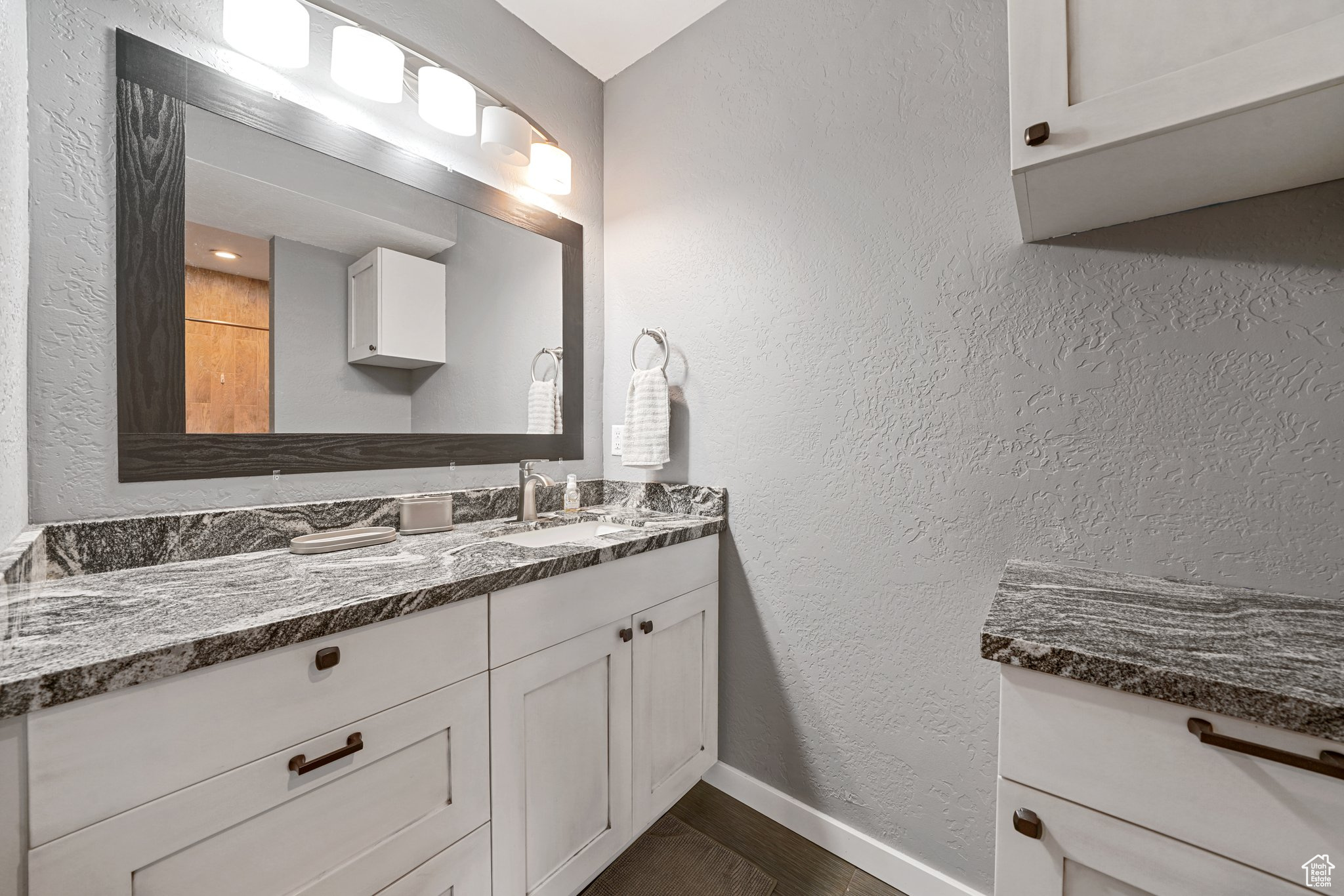 Bathroom featuring vanity, wood finished floors, a textured wall, and baseboards