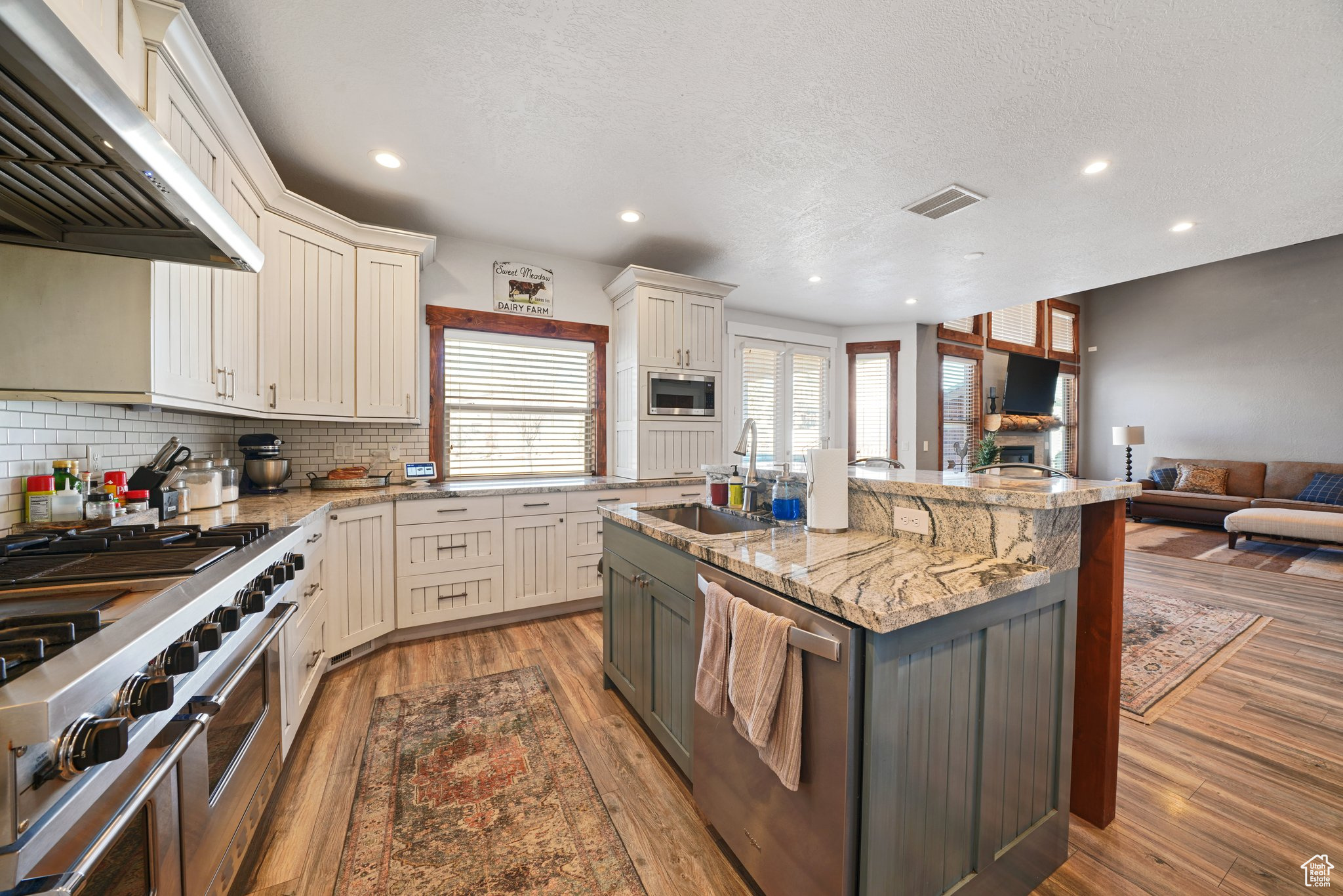 Kitchen with range hood, visible vents, a sink, stainless steel appliances, and open floor plan