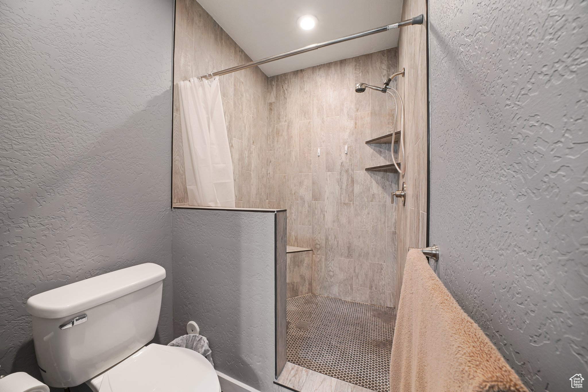 Bathroom with tiled shower, toilet, and a textured wall